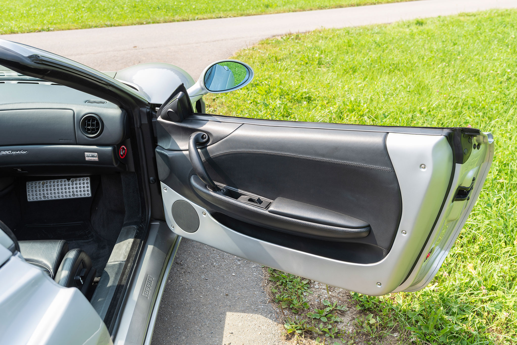 La porte s’ouvre largement pour pouvoir se glisser dans le siège baquet recouvert de cuir noir – Ferrari 360 Spider. La porte s’ouvre largement pour pouvoir se glisser dans le siège baquet recouvert de cuir noir – Ferrari 360 Spider.